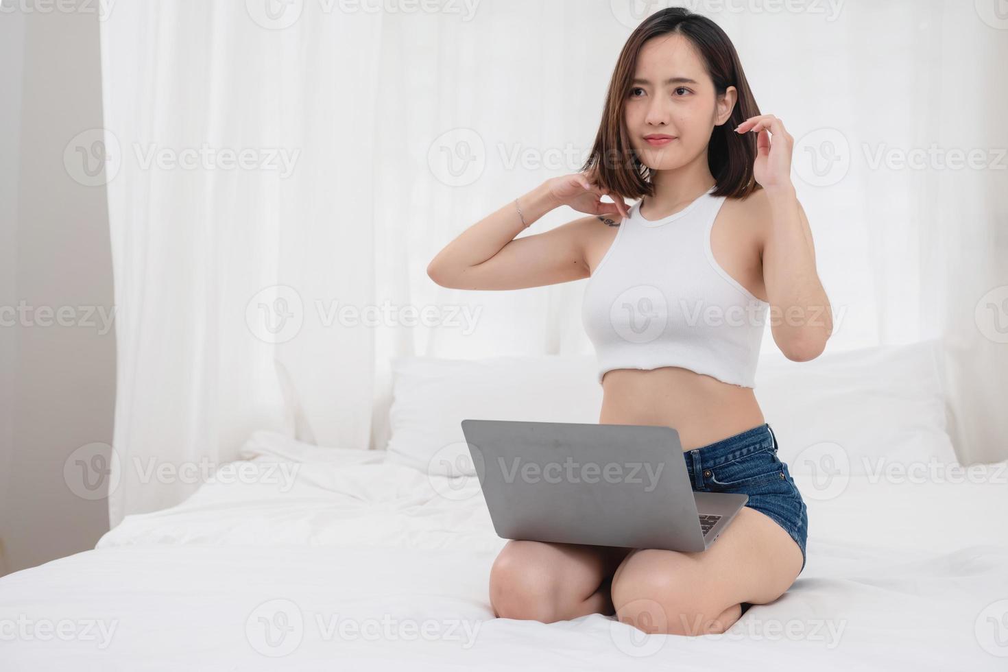 Portrait of a white Asian woman with a tattoo sitting resting on a bed and playing laptop for a working holiday, vacation concept. photo