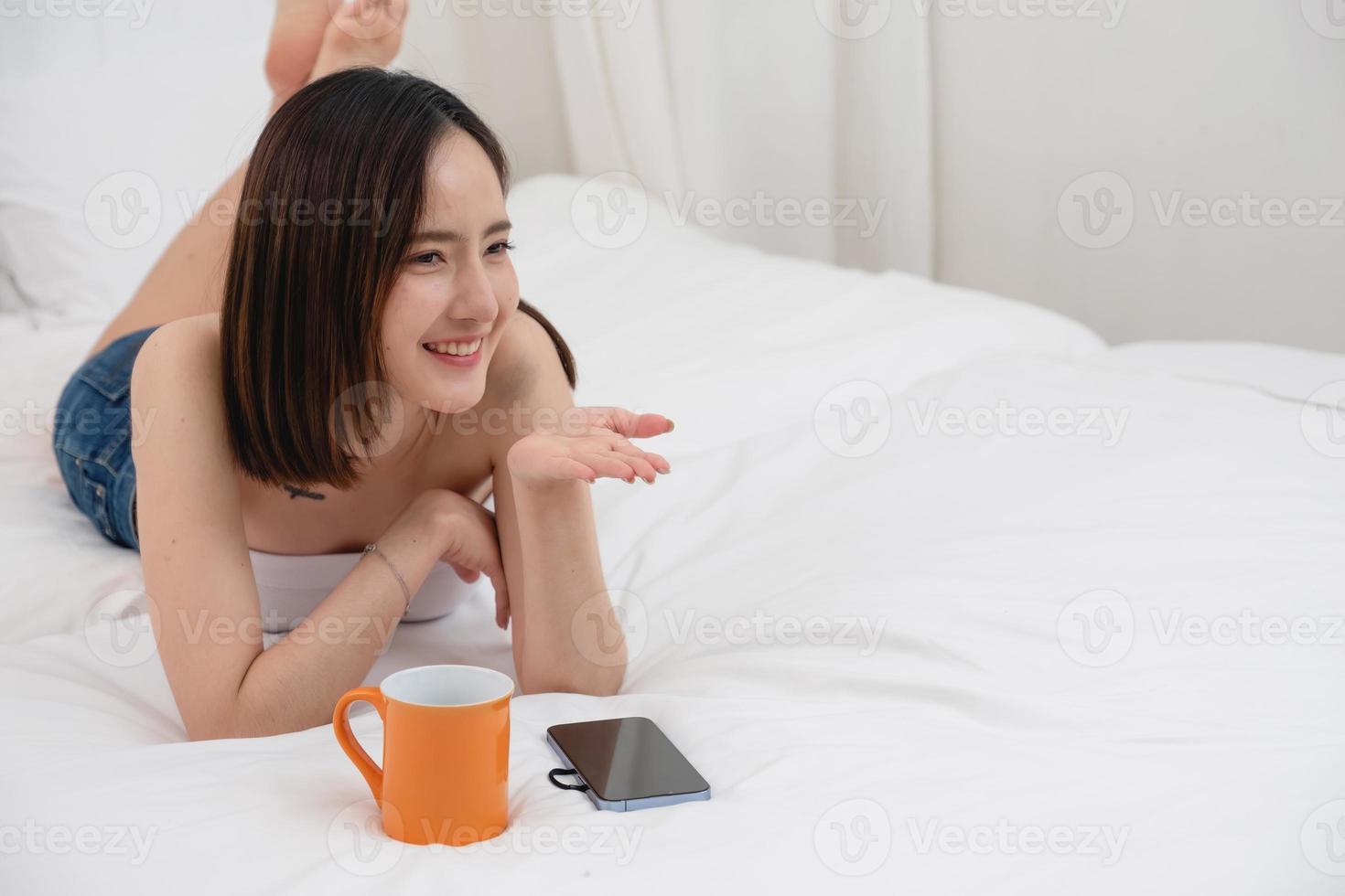 Portrait of white Asian woman with tattoo resting in bed to rest and relax inside white bedroom on her holiday, holiday morning concept. photo