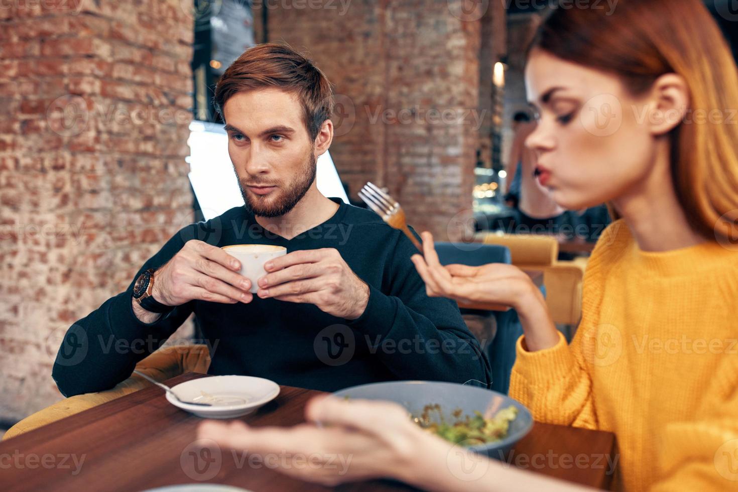 woman having dinner at a table in a cafe and a man with a cup of coffee in the background photo
