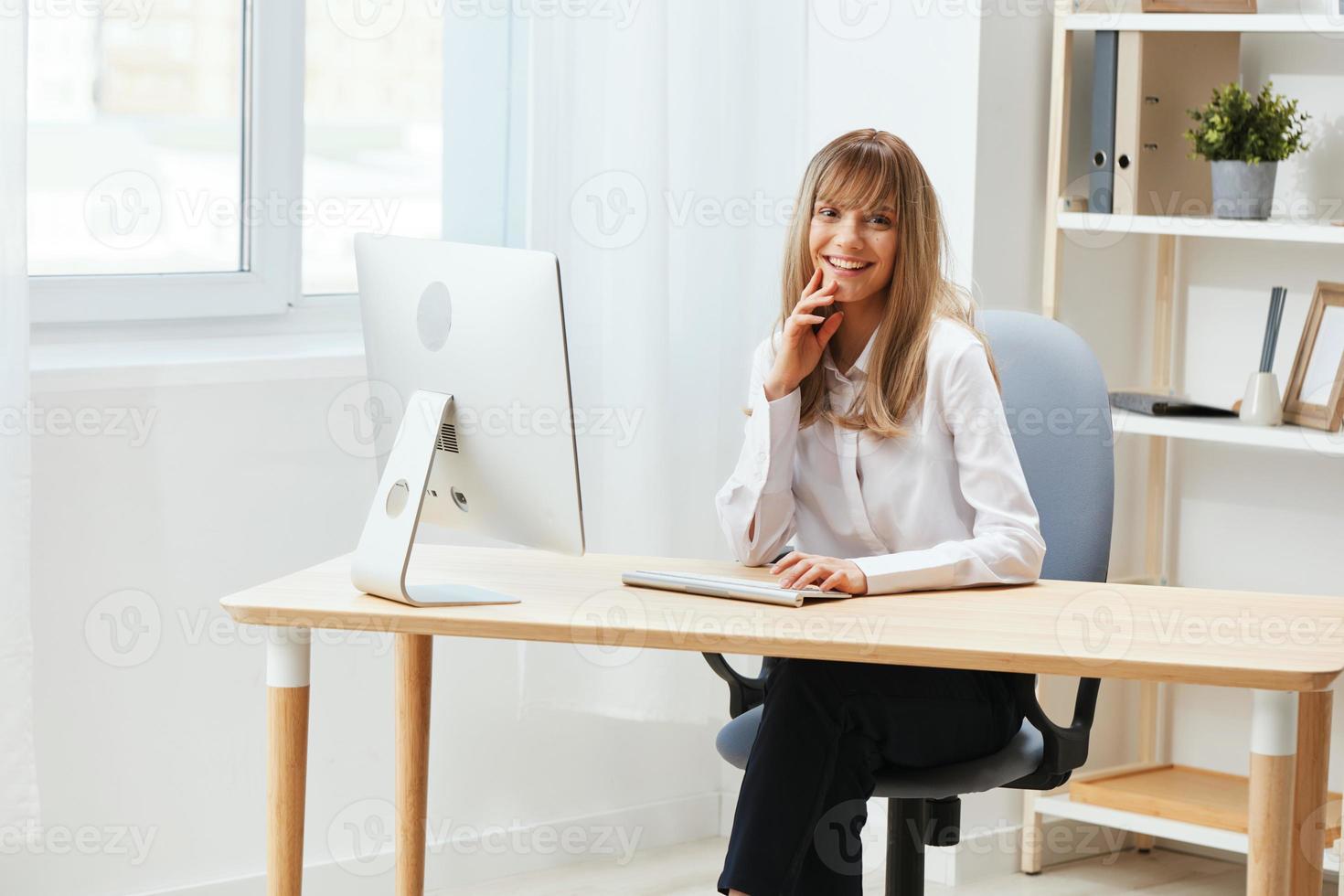 Happy smiling adorable blonde businesswoman worker freelancer look at camera sitting at workplace in light modern office. Cheerful employee work on computer online in support service. Copy space photo