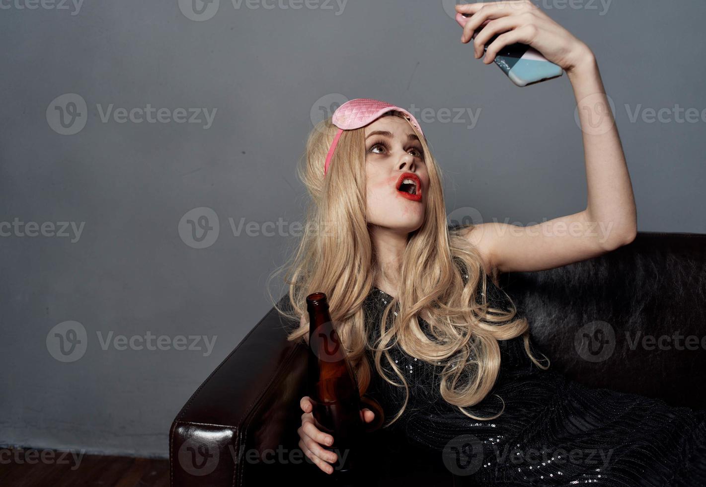 un borracho mujer en el sofá es tomando imágenes de sí misma en un célula teléfono foto