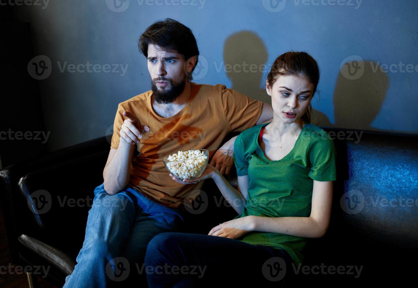 A woman and a man with popcorn on a leather sofa indoors watching TV in the evening photo