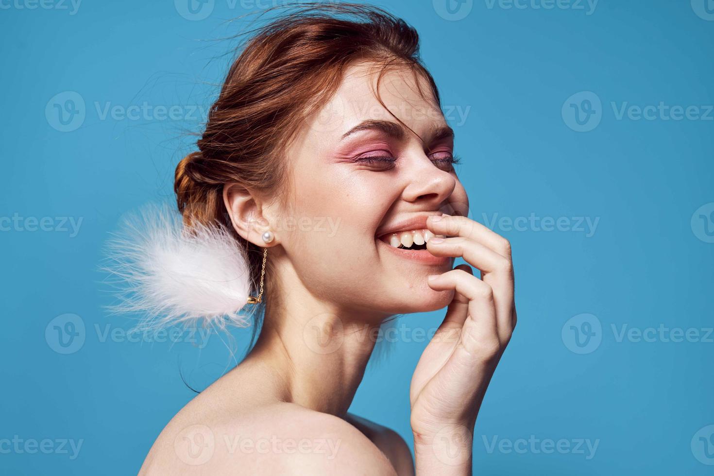 pretty woman naked shoulders and fluffy earrings bright makeup blue background photo