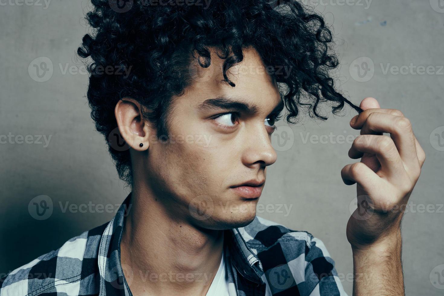 man examines his locks of hair and gray background plaid shirt handsome guy model photo