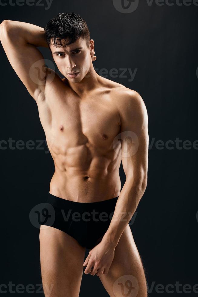 man with pumped up abs hold hands above his head in a dark background photo