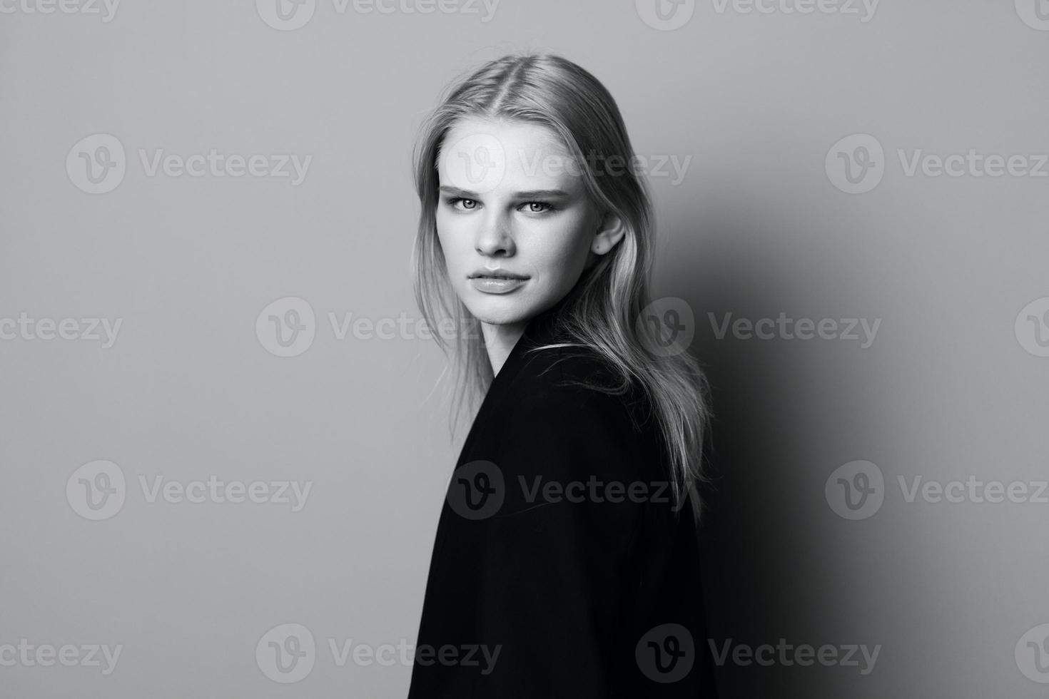 Young expressive beautiful blonde professional model posing isolated in studio dressing in black jacket looks at camera. Fashion Minimalistic concept photo