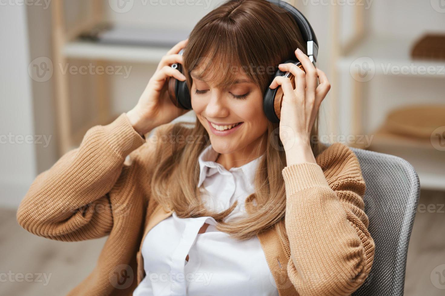 linda contento joven rubia estudiante dama persona de libre dedicación en calentar suéter vestir auriculares disfrutar fav canciones sentado en Sillón a moderno hogar interior. música hora relajante frio lista de reproducción concepto. Copiar espacio foto