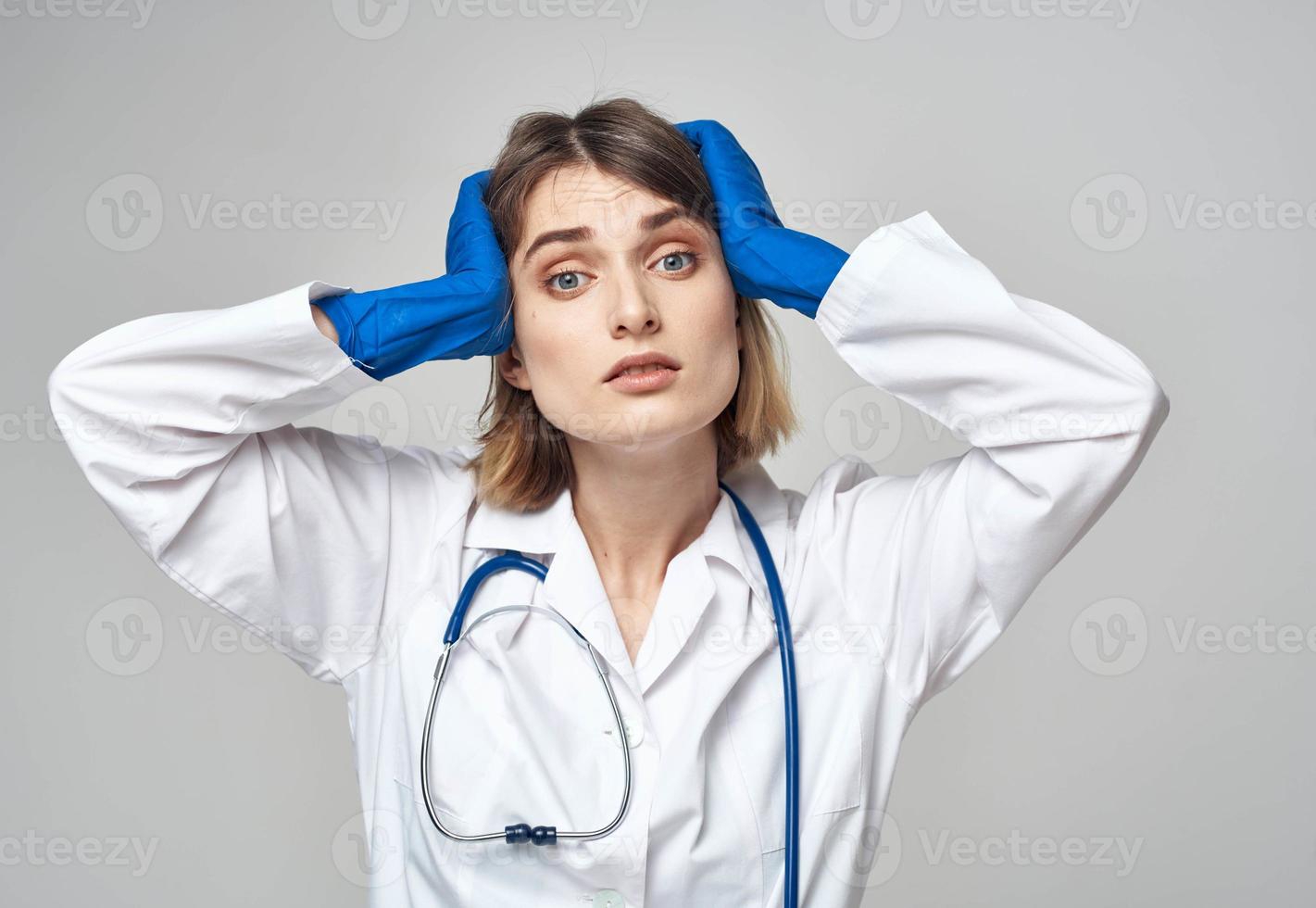emocional mujer en azul médico guantes toques su cabeza con su manos foto