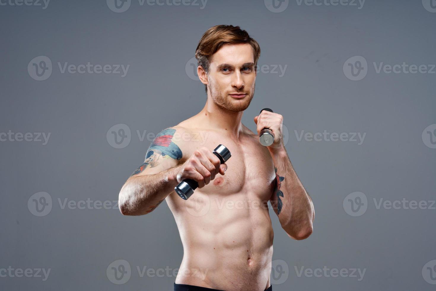 desnudo atleta con un tatuaje y pesas en manos teléfono aptitud culturismo foto