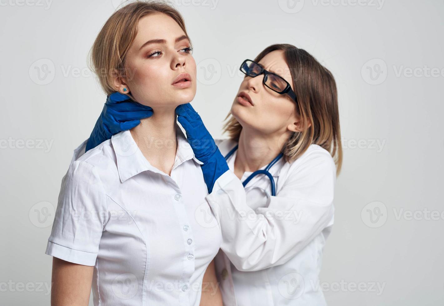 un mujer médico en un médico vestido y azul guantes examina el del paciente cara foto