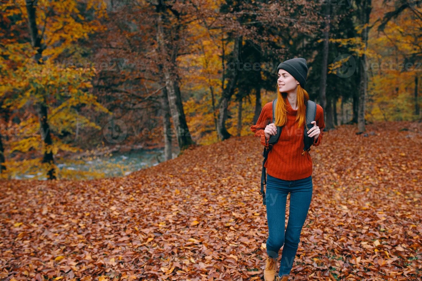 viajero con un mochila en el otoño bosque y sombrero suéter pantalones caído hojas lago arboles foto