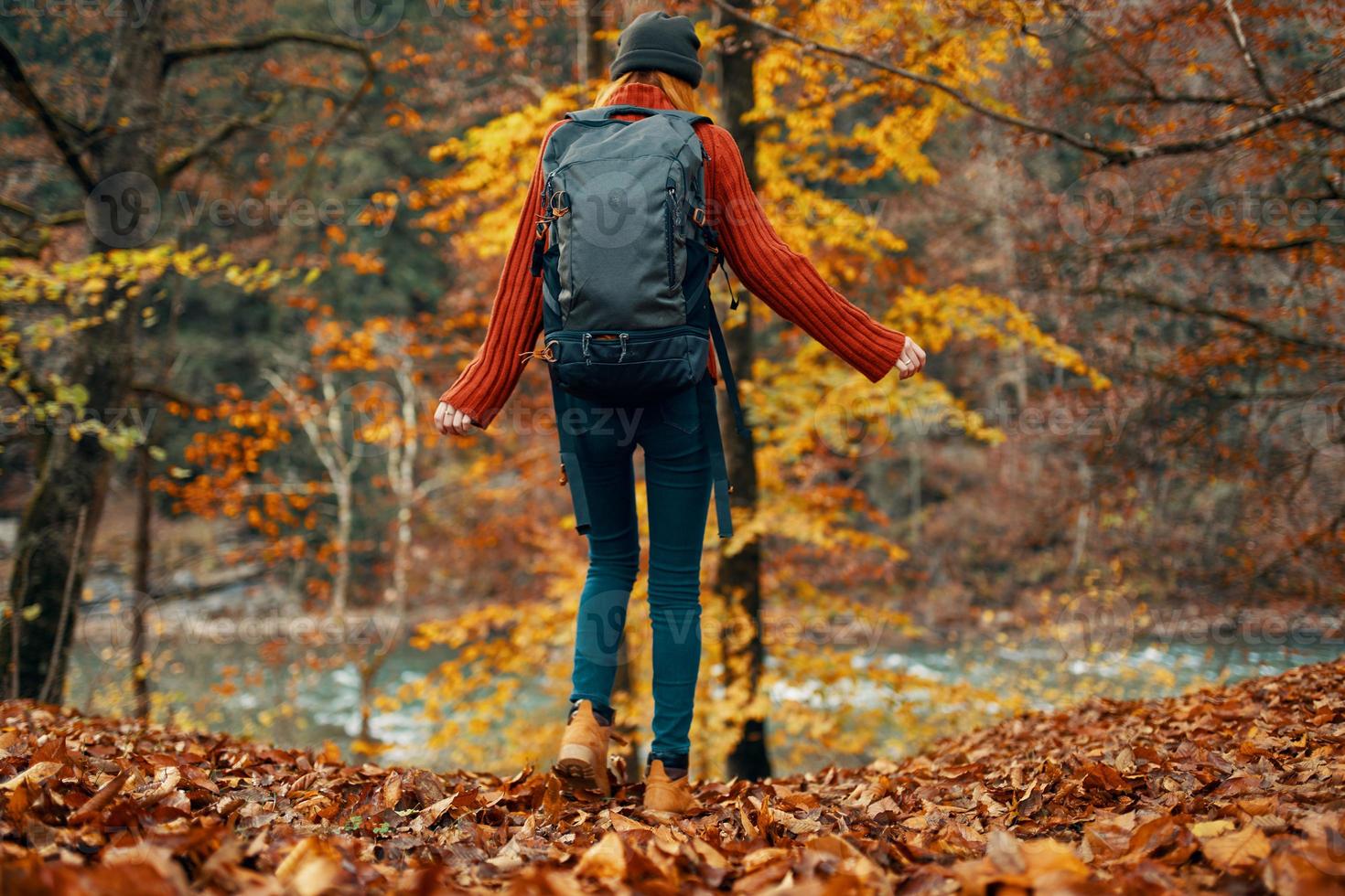 young woman in jeans and a sweater with a backpack on her back walks in the park in autumn in nature, bottom view photo