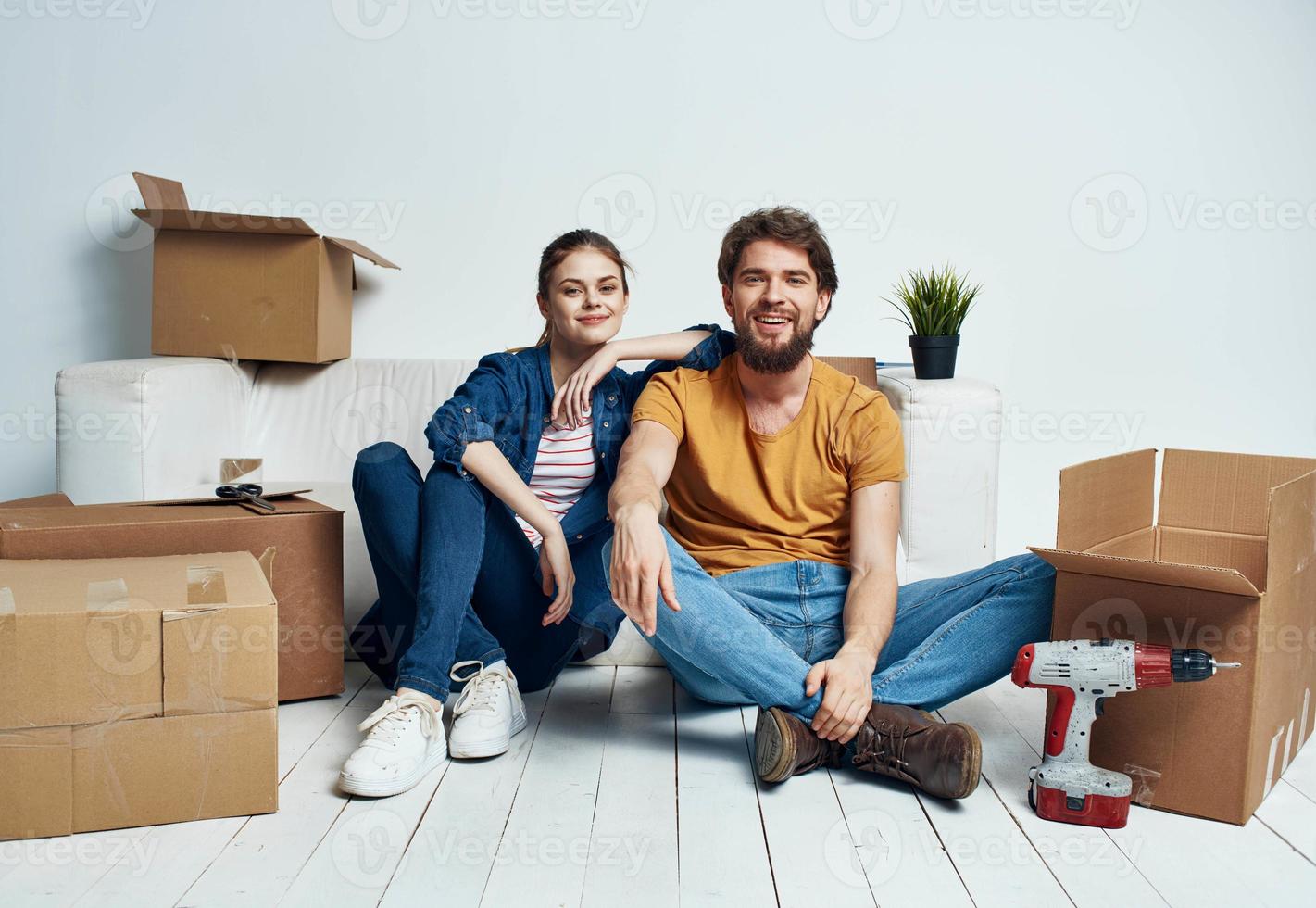 A man and a woman are sitting on the floor indoors near the couch and moving boxes photo