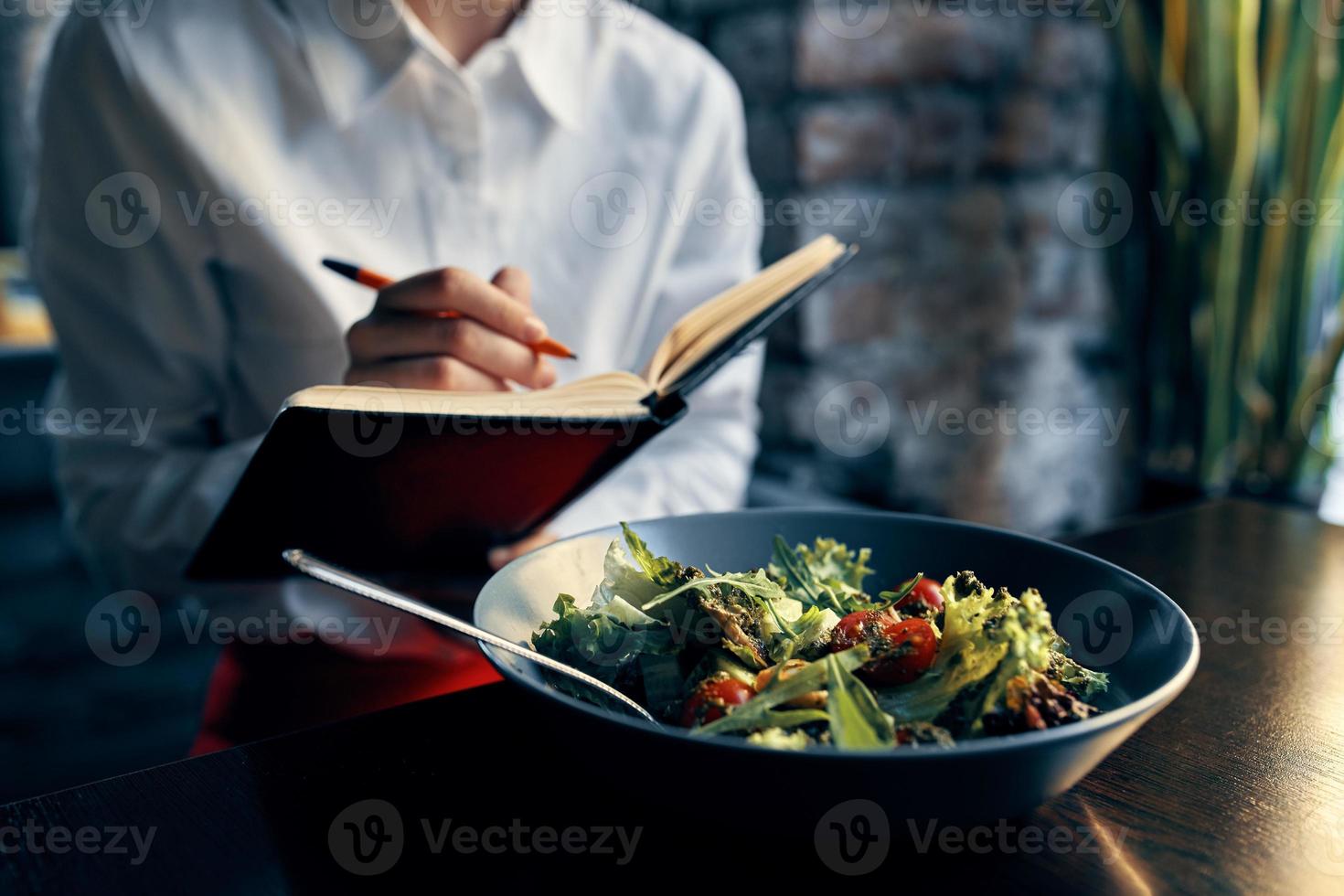 woman with notepad near the window and salad in a plate tomatoes fresh vegetables photo