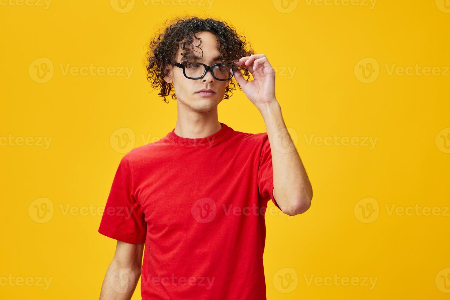 Cute attractive myopic young student man in red t-shirt hold funny eyewear posing isolated on over yellow studio background. The best offer with free place for advertising. Education College concept photo