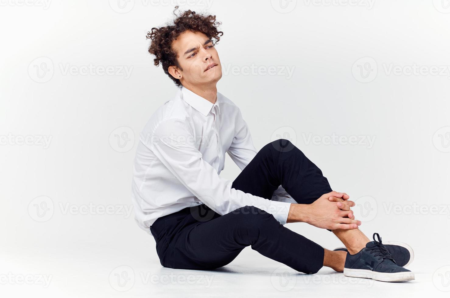 un adolescente en un traje y zapatillas se sienta en el piso en un brillante habitación lado ver foto