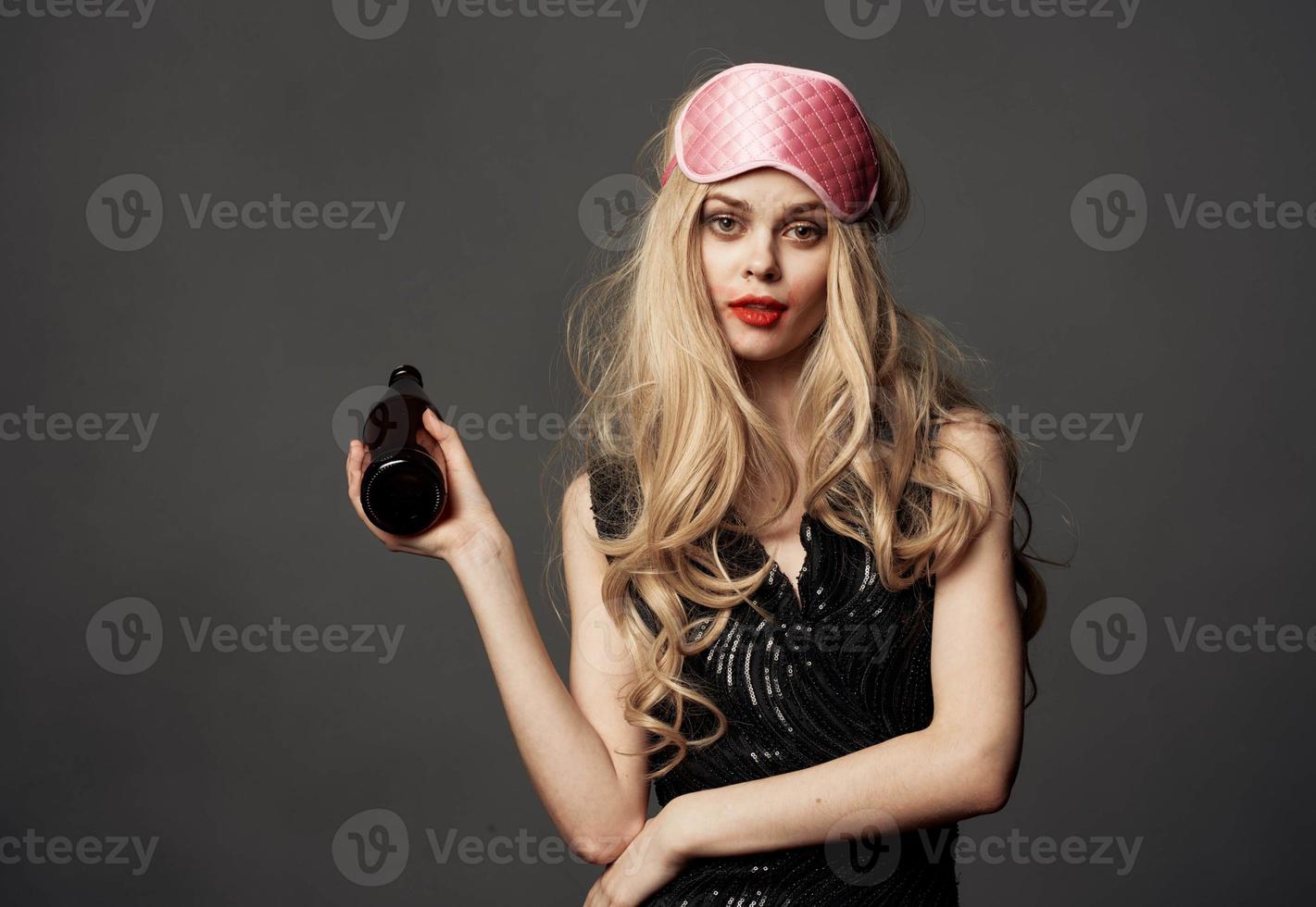 Women with a pink sleep mask holds a bottle of beer in her hand photo