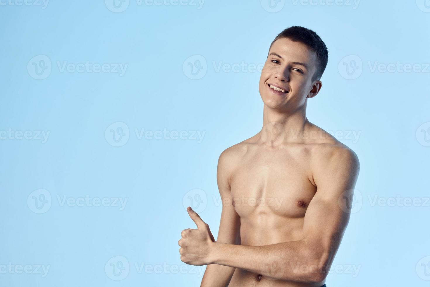 guy with pumped up abs shows thumb on blue background photo