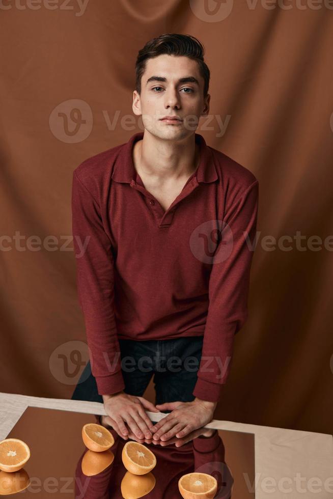 An attractive young man stands near a table with a mirror and oranges photo