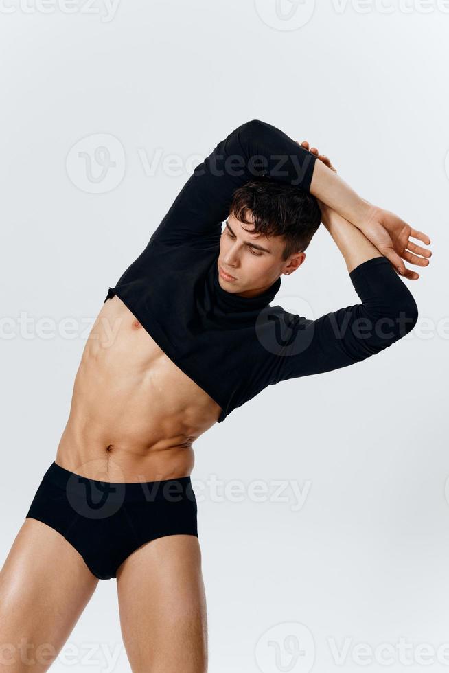 a young man with a pumped-up torso in shorts and a sweater bent over to the side on a light background photo