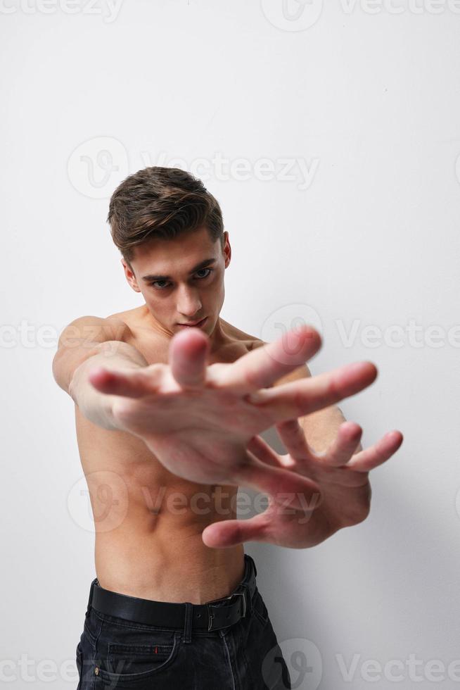 A man with a naked torso gestures with his hands in front of his face against a light background cropped view photo