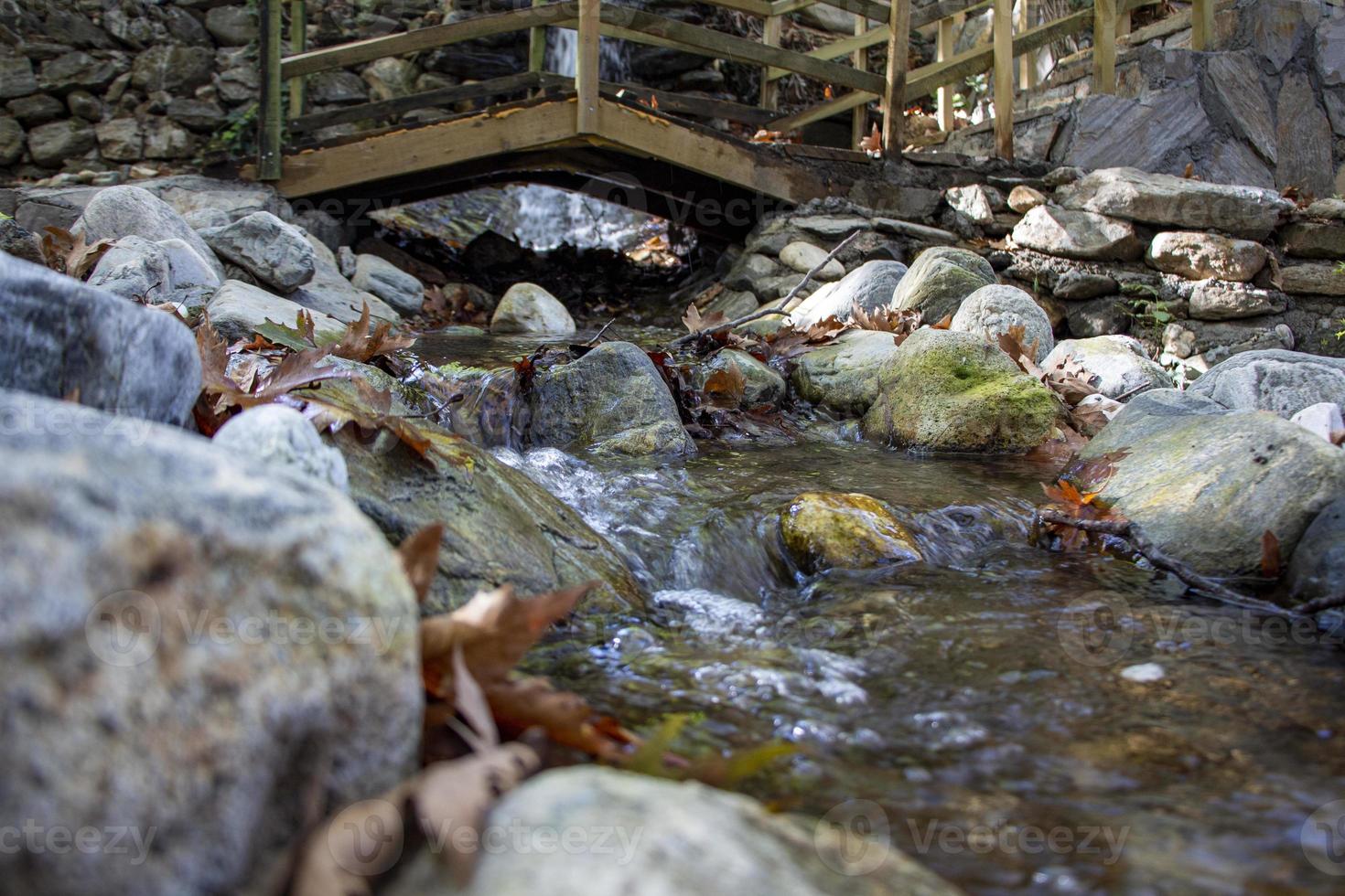 Wooden bridge over a small stream in the forest. Waterfall in the garden with rocks and leaves in the autumn season. Wooden bridge over a stream in the garden of a country house photo