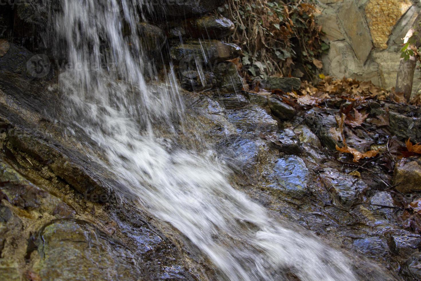 Waterfall in the autumn forest with fallen leaves on the rocks. Small waterfall in the forest. Mountain landscape. photo