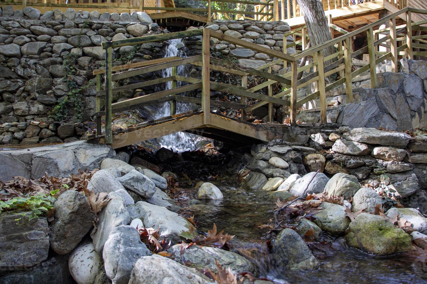 Wooden bridge over a small stream in the forest. Waterfall in the garden with rocks and leaves in the autumn season. Wooden bridge over a stream in the garden of a country house photo