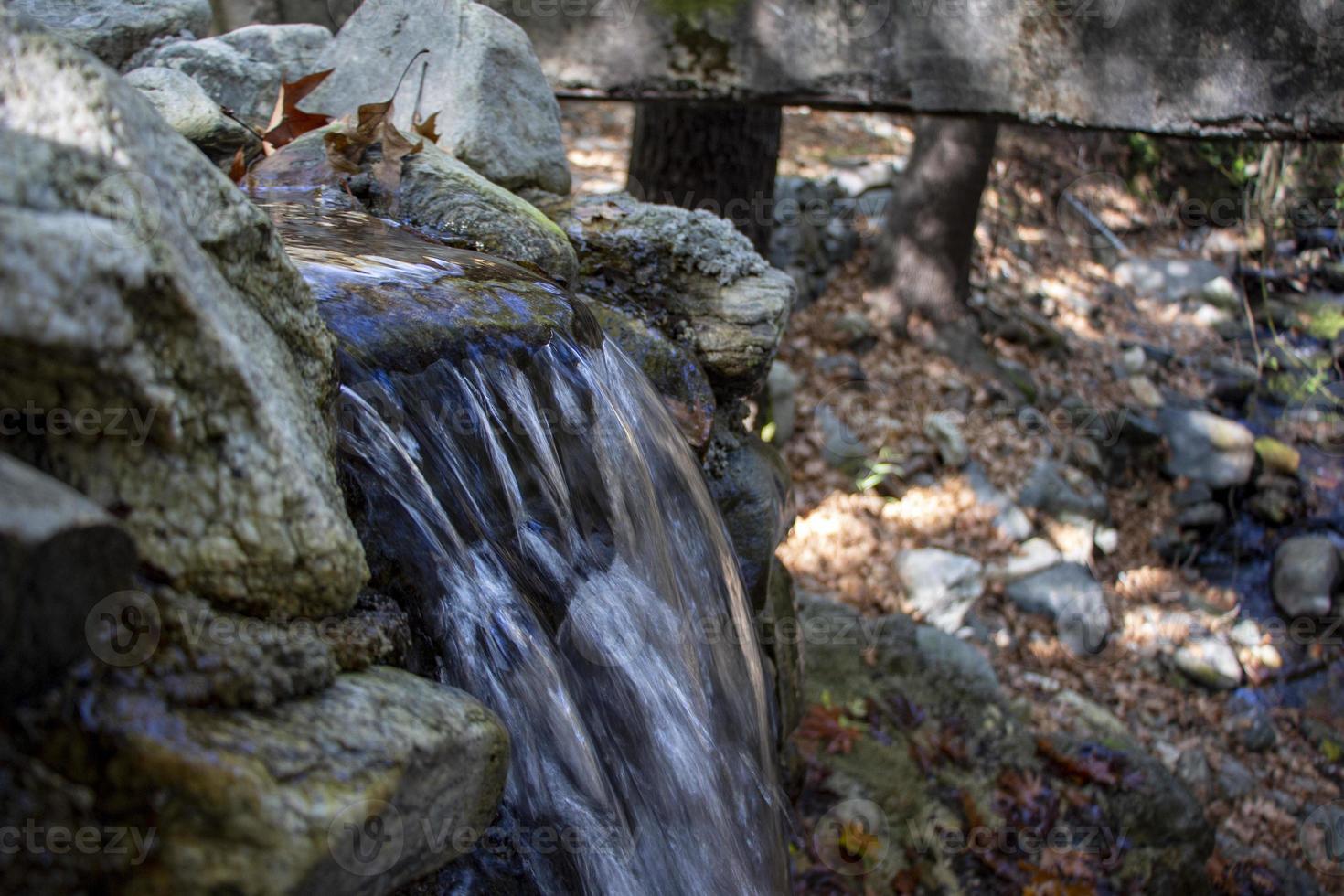 Waterfall in the autumn forest with fallen leaves on the rocks. Small waterfall in the forest. Mountain landscape. photo