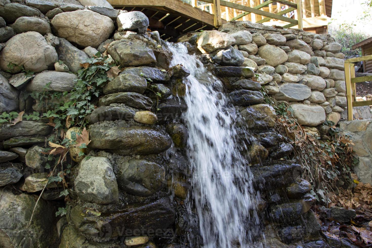 Waterfall in the autumn forest with fallen leaves on the rocks. Small waterfall in the forest. Mountain landscape. photo