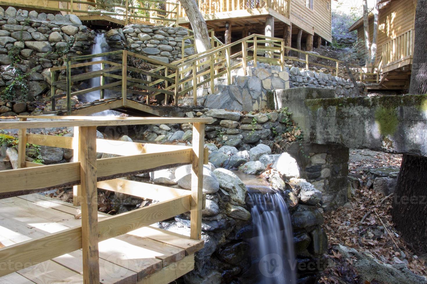 Waterfall in the park. Water cascades down the stairs. Waterfall in the forest with wooden stairs and railings in the mountains photo