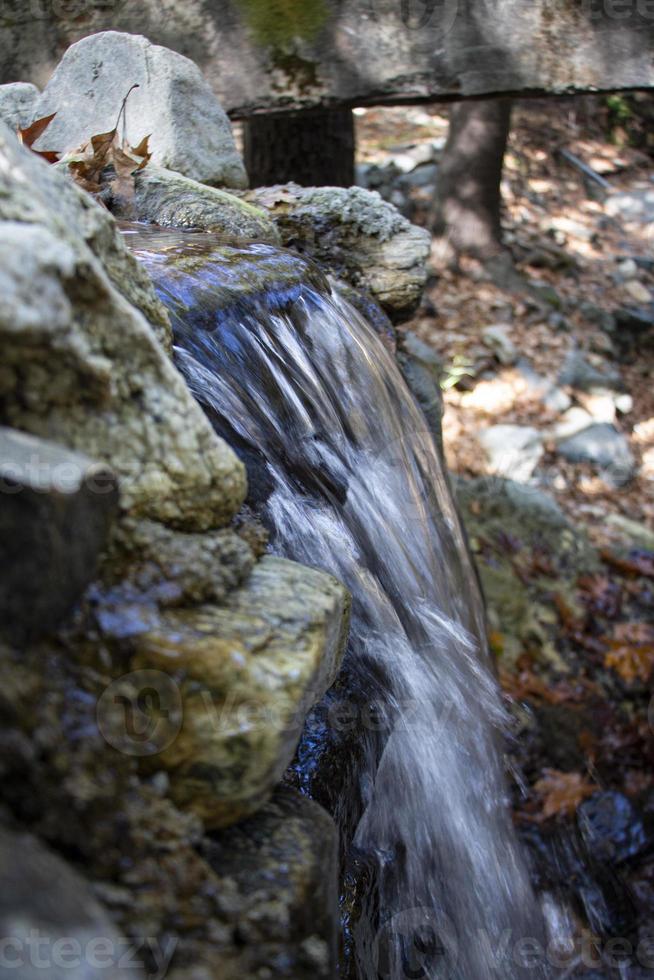 Waterfall in the autumn forest with fallen leaves on the rocks. Small waterfall in the forest. Mountain landscape. photo