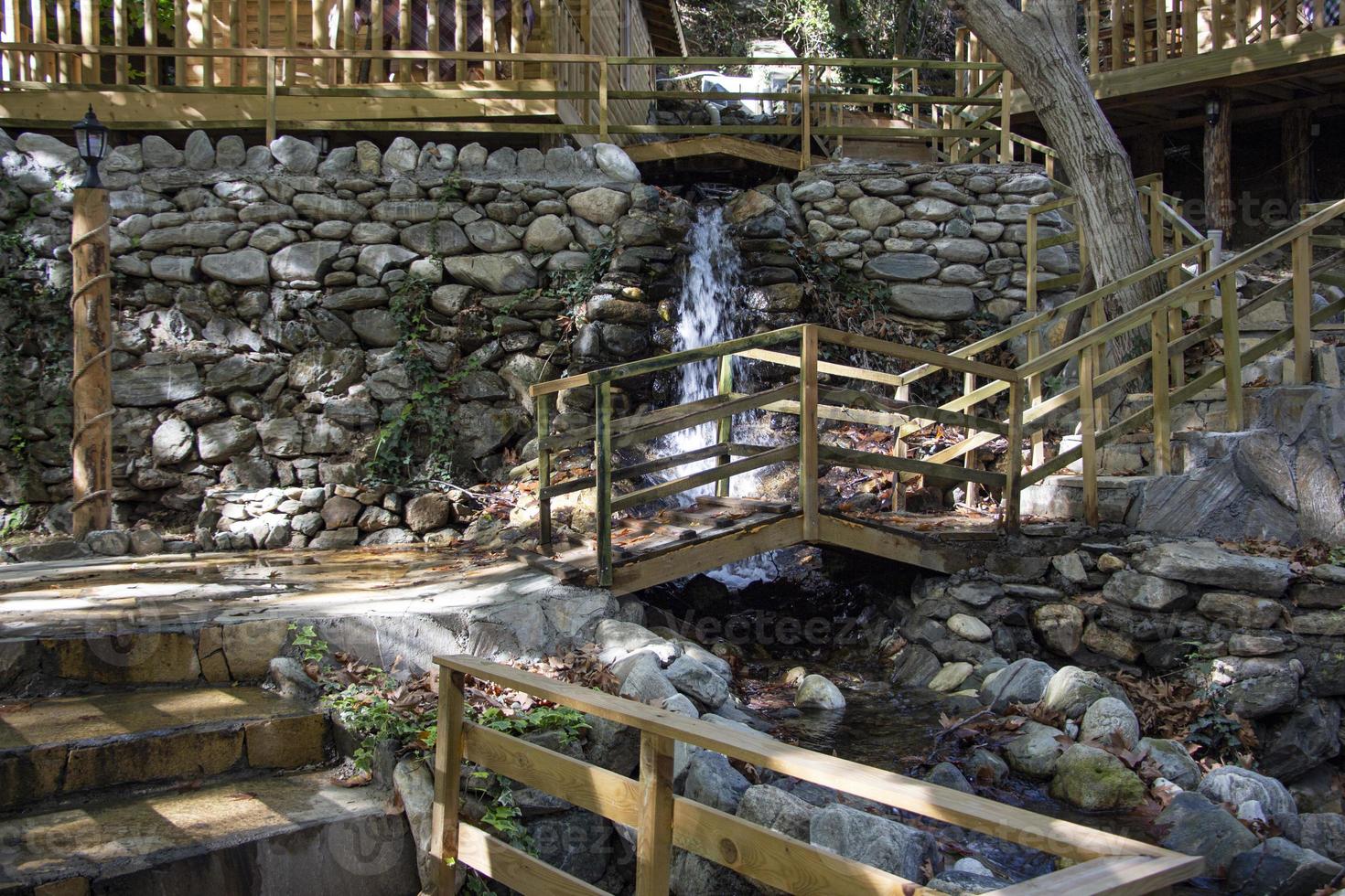 Waterfall in the park. Water cascades down the stairs. Waterfall in the forest with wooden stairs and railings in the mountains photo