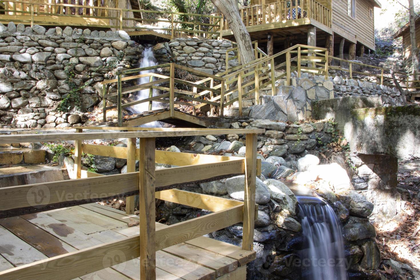 Waterfall in the park. Water cascades down the stairs. Waterfall in the forest with wooden stairs and railings in the mountains photo