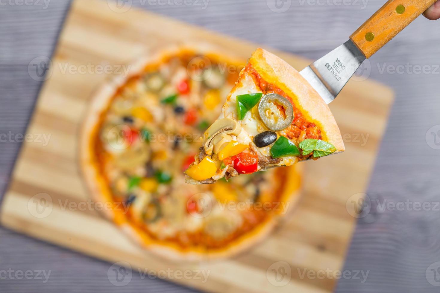 Close up and top view of Chicken mushroom jalapeno pizza slice lifted from wooden cutting board. photo