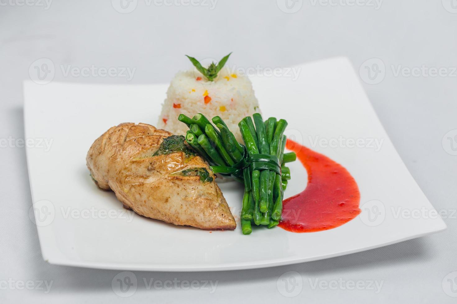 Pan roasted chicken breast with long green beans and light vegetable rice platter. Food decorating with red sauce on a white plate. Isolated white background. photo