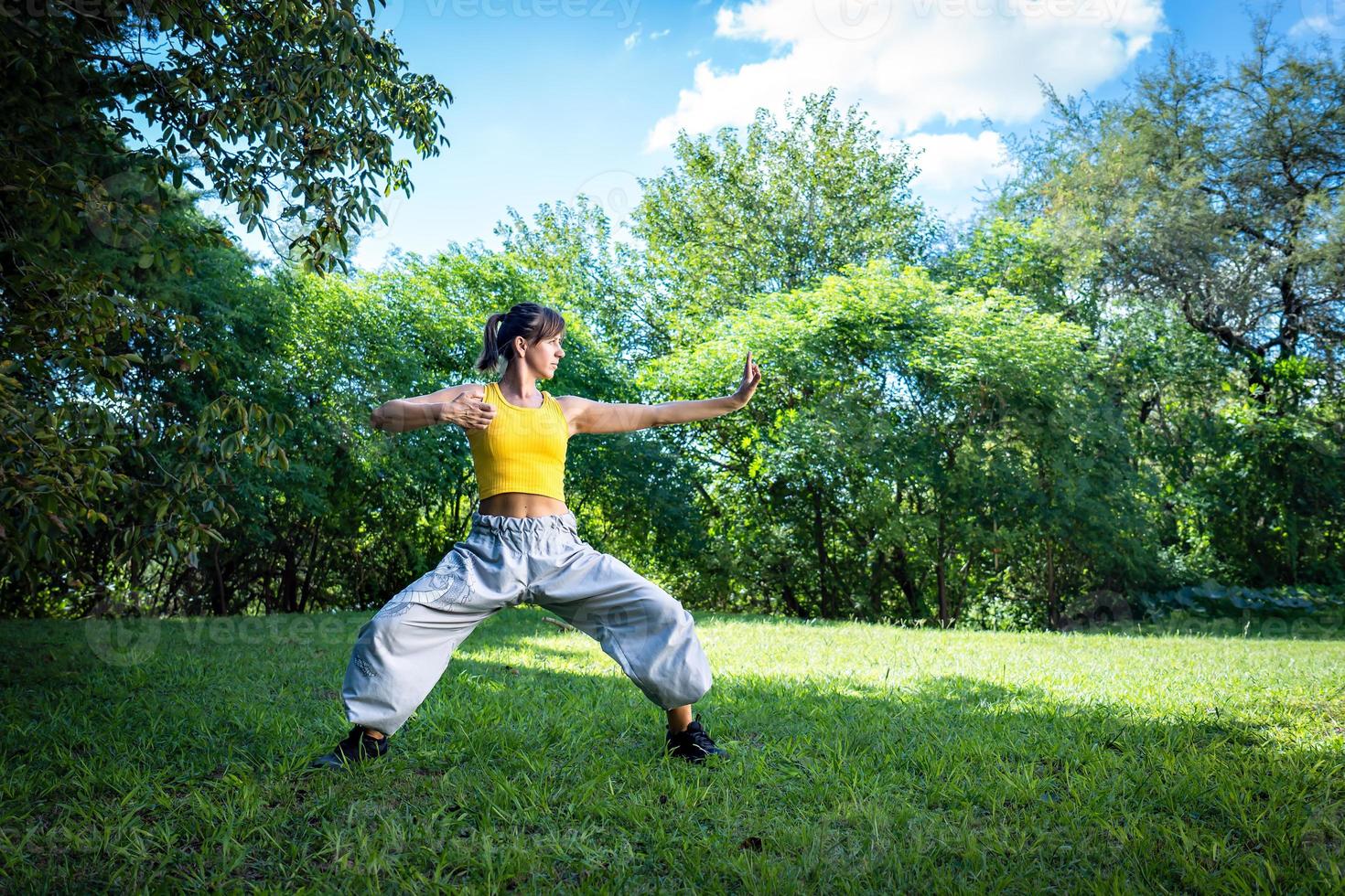 Woman practices Tai Chi outdoor, provides additional health benefits, such as exposure to the sun for vitamin D production and connection with nature to reduce stress and improve emotional well-being. photo