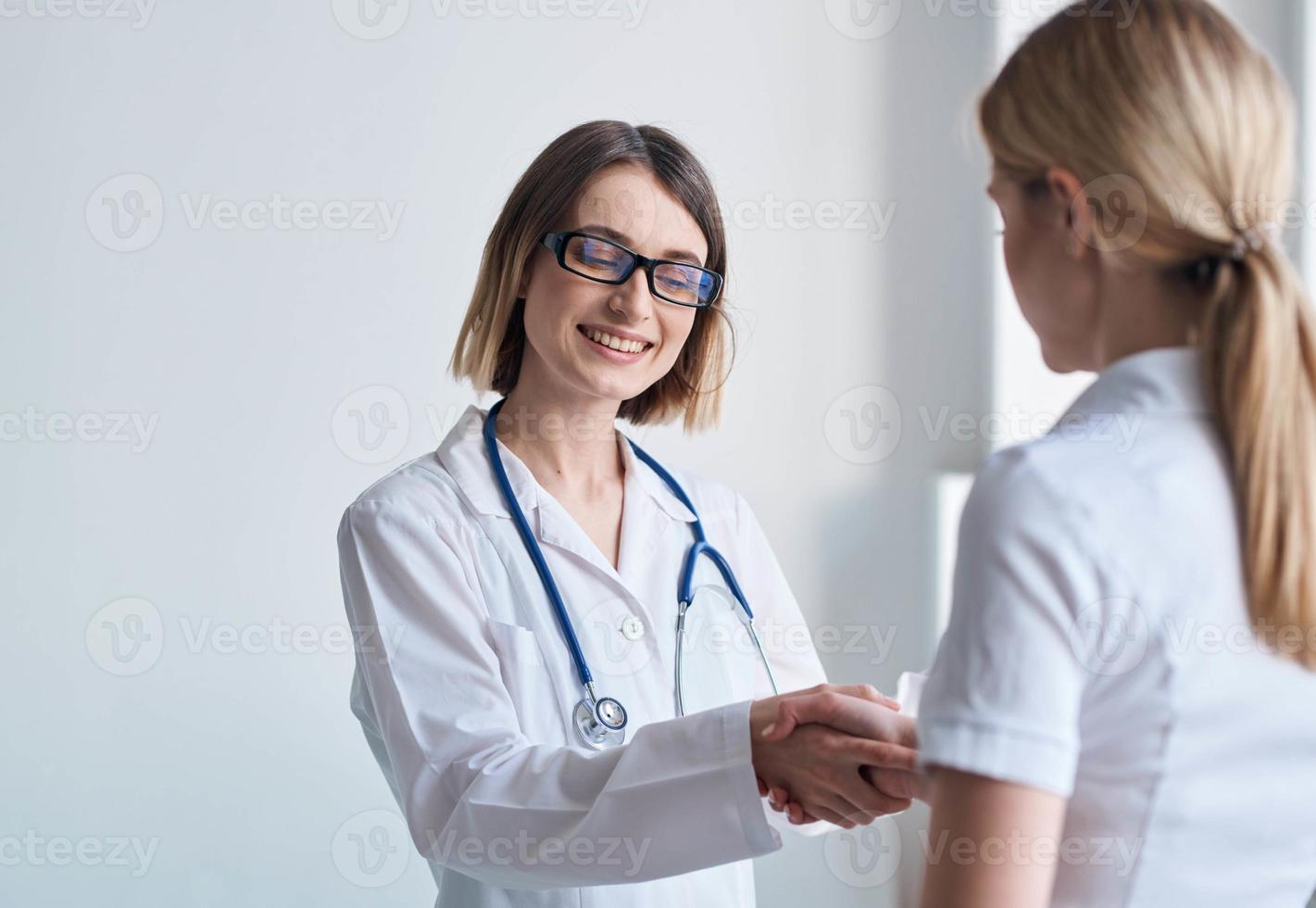 mujer médico batidos manos con paciente en blanco camiseta foto