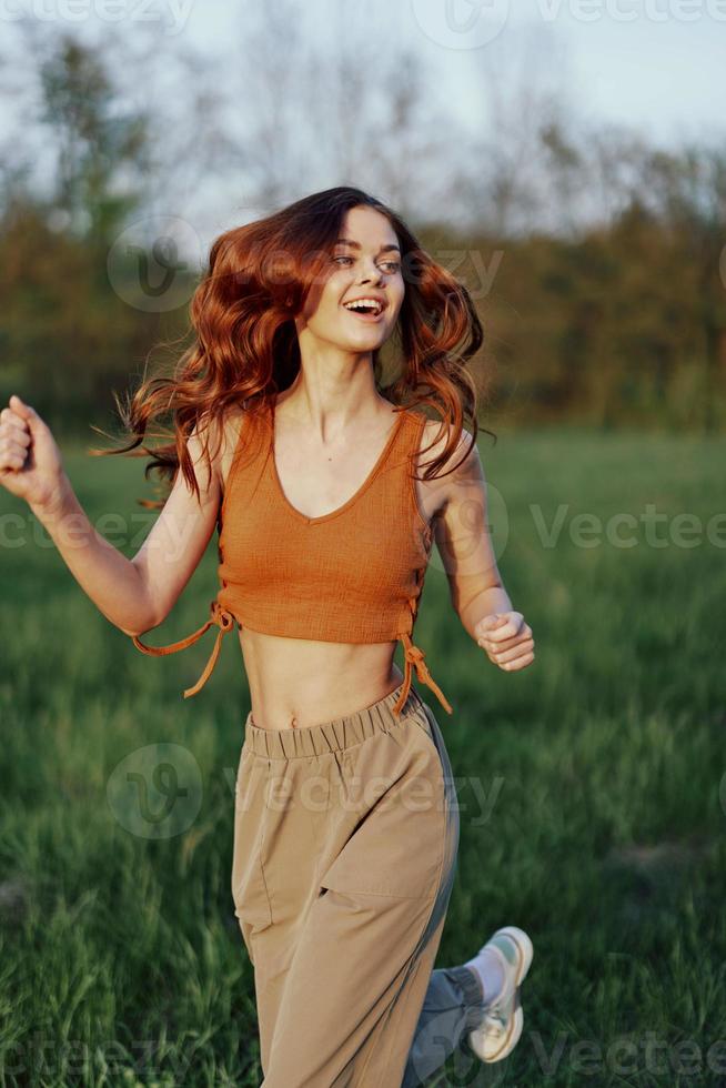 un contento atlético mujer es trotar y sonriente en naturaleza en el parque, verano puesta de sol ligero foto