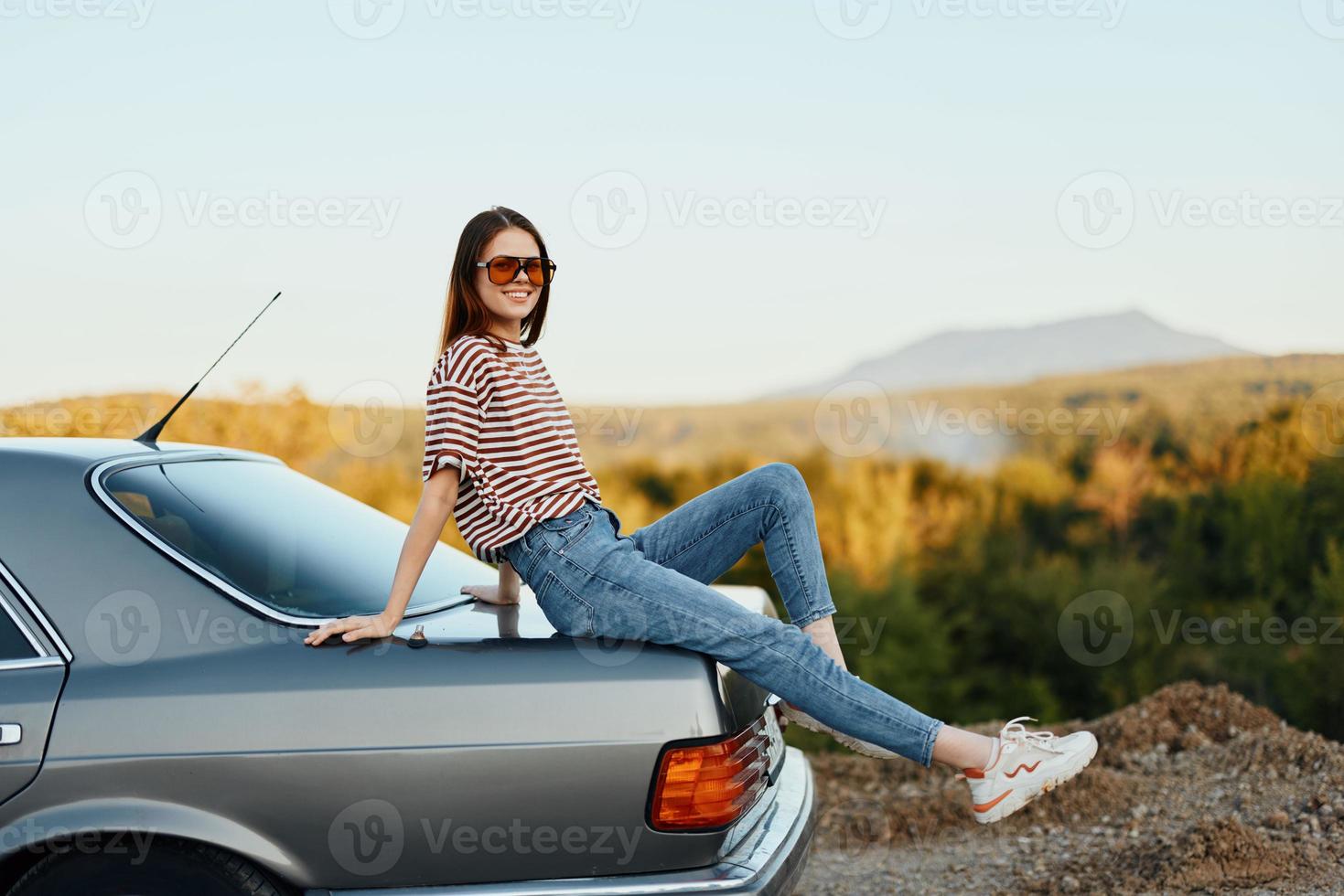 A woman with a car stopped on the road to rest on the journey raised her arms and legs from happiness and a beautiful landscape photo