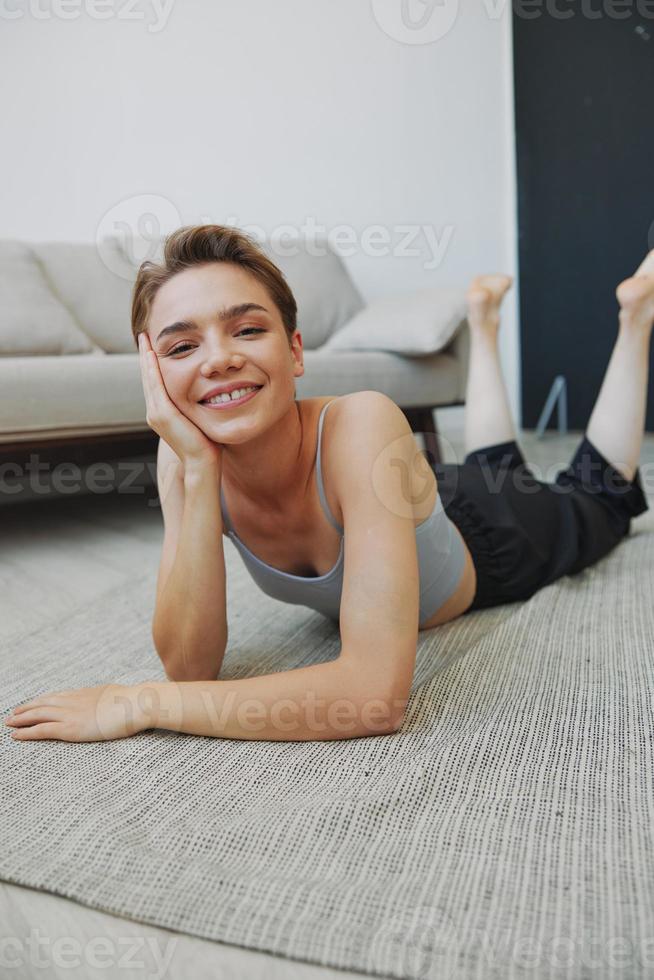 Teenage girl lying on the floor at home smiling in home clothes with a short haircut, lifestyle without filters, free copy space photo