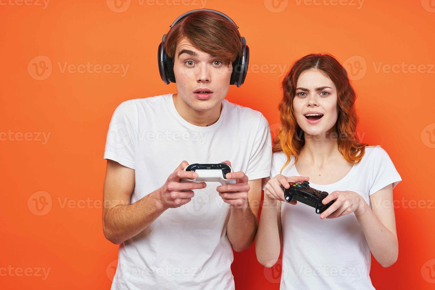 young couple in white t-shirts with joysticks playing a console orange background photo