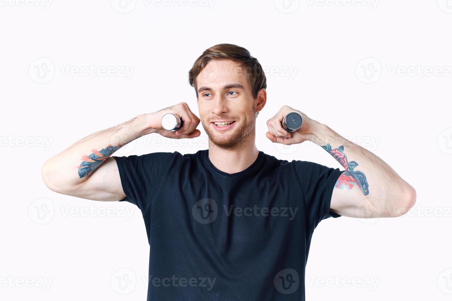 guy with dumbbells holds his hand behind his head and light background black t-shirt sport fitness photo