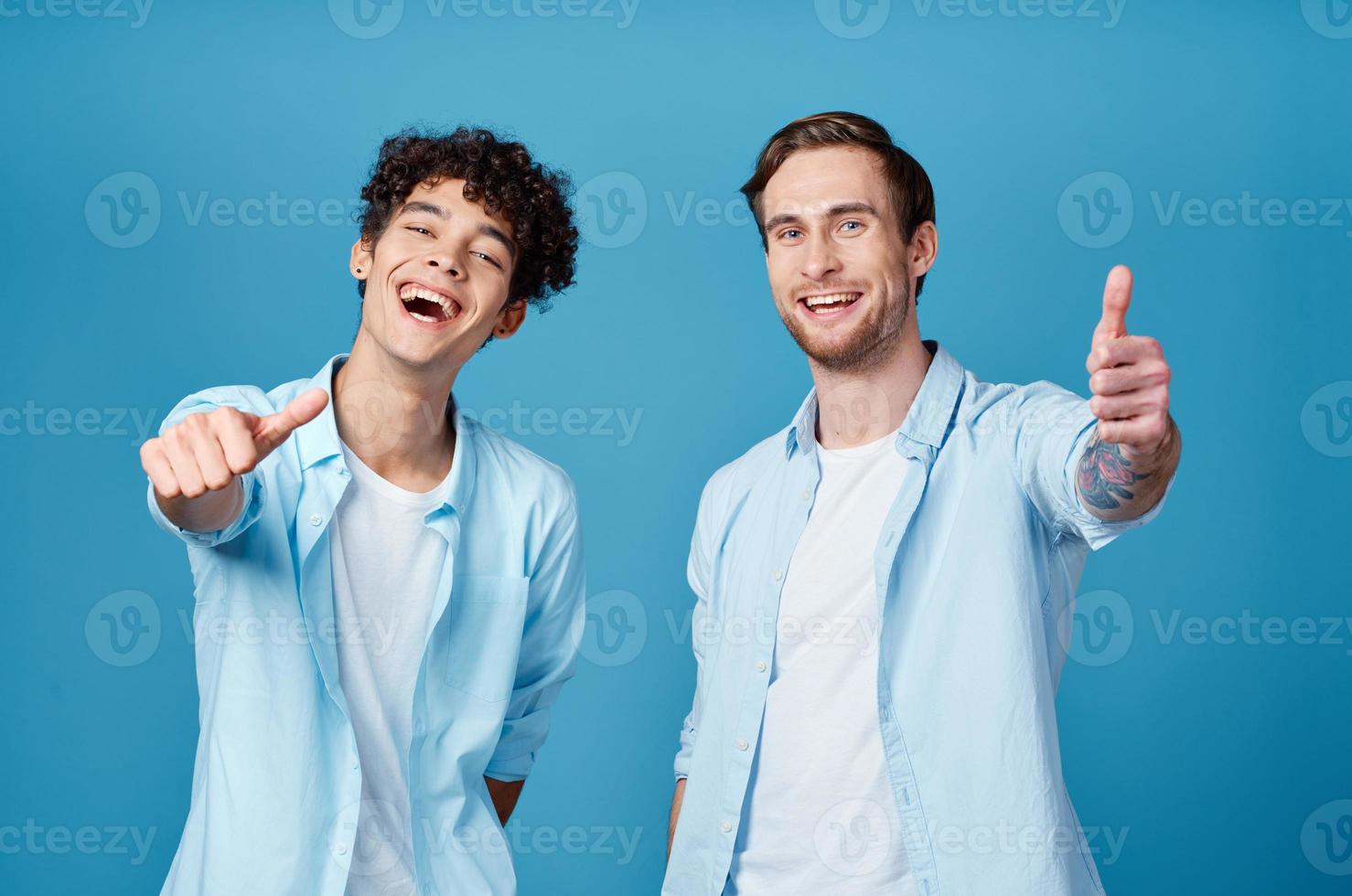 two friends in identical shirts and a t-shirt gesturing with their hands on a blue background photo