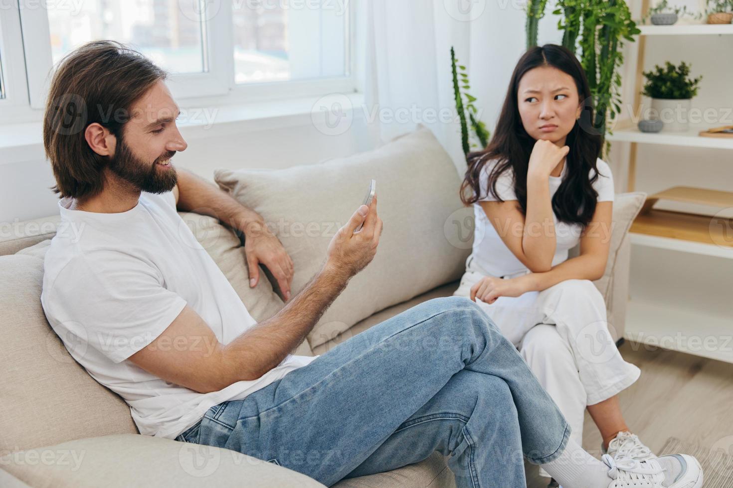 A man looks at the phone screen during an argument with his girlfriend. The angry and hurt woman looks in his direction and is sad. Family discord at home, phone addiction photo