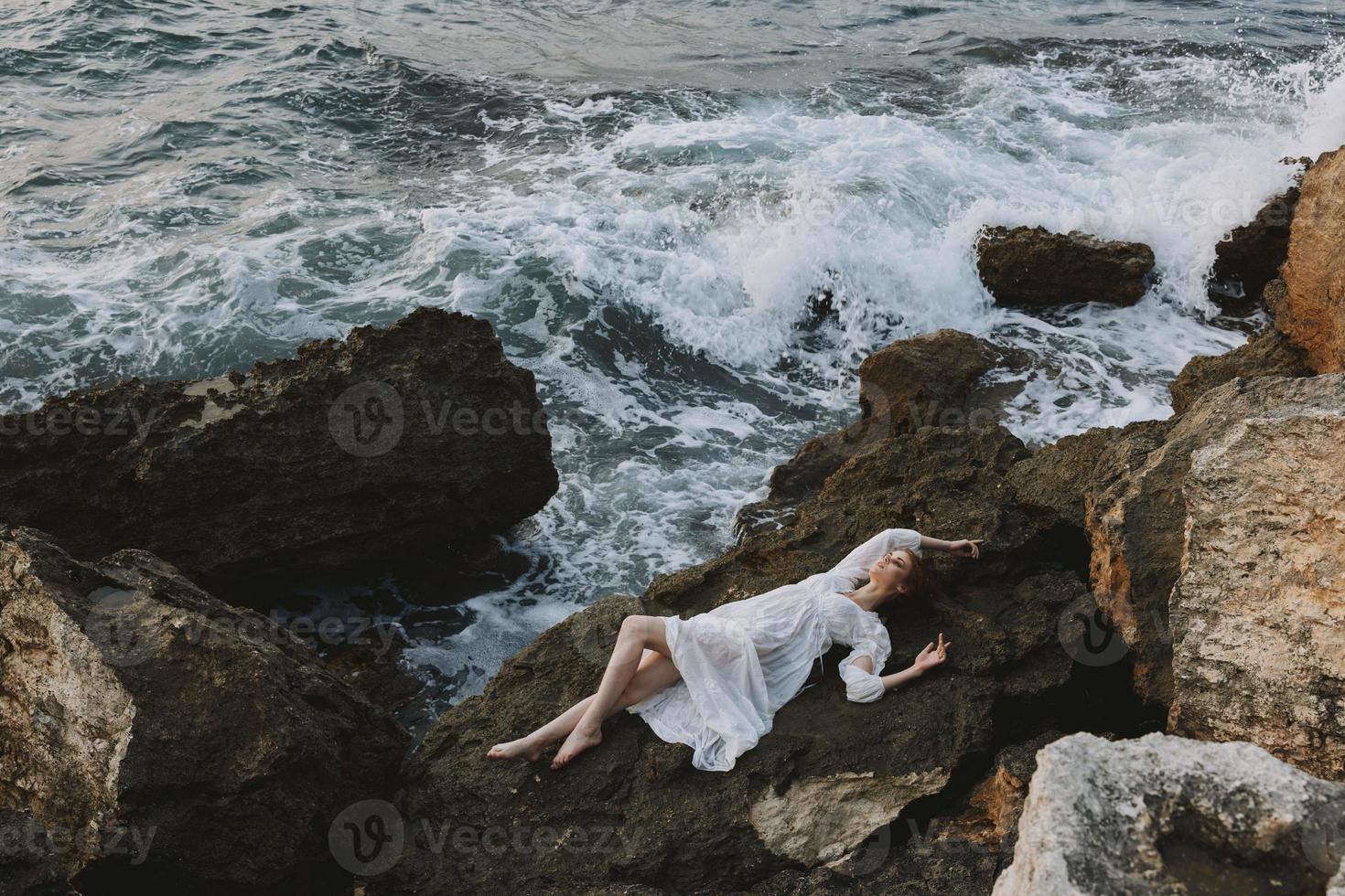 atractivo mujer con largo pelo acostado en rocoso costa con grietas en rocoso superficie vacaciones concepto foto