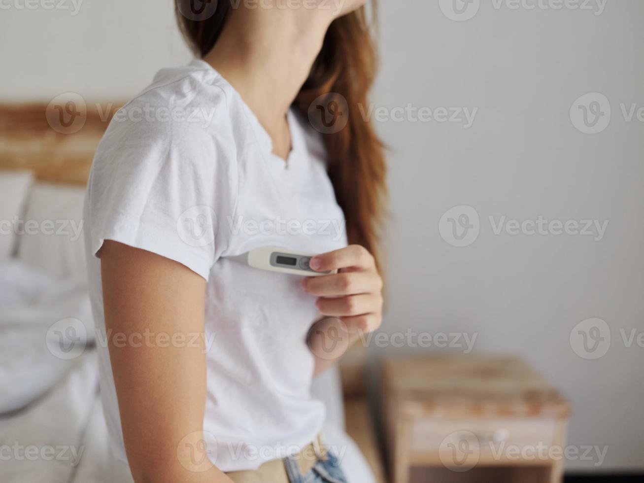 woman holding a thermometer under her arm in the bedroom photo