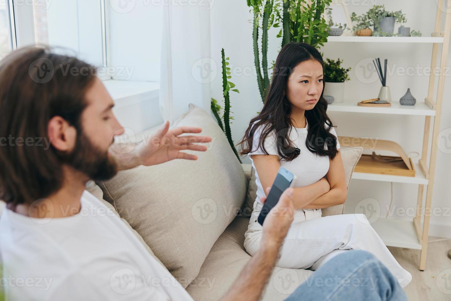 A man looks at the phone screen during an argument with his girlfriend. The angry and hurt woman looks in his direction and is sad. Family discord at home, phone addiction photo