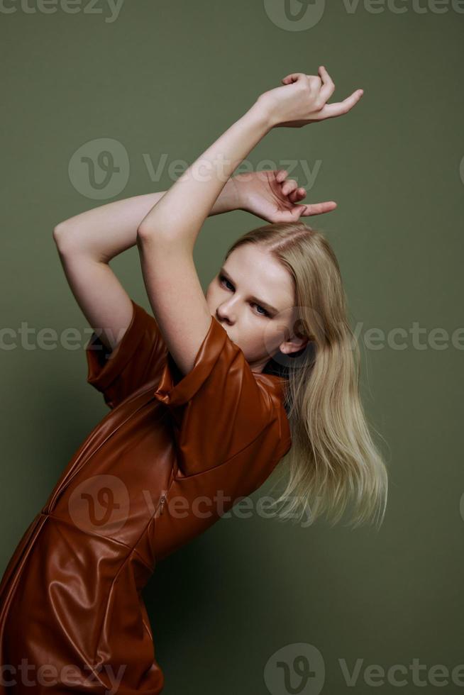 Fashion Art banner. Curving in dance blonde young female model in brown trendy dress holding hands up confident looks at camera posing isolated on over olive green studio wall background photo