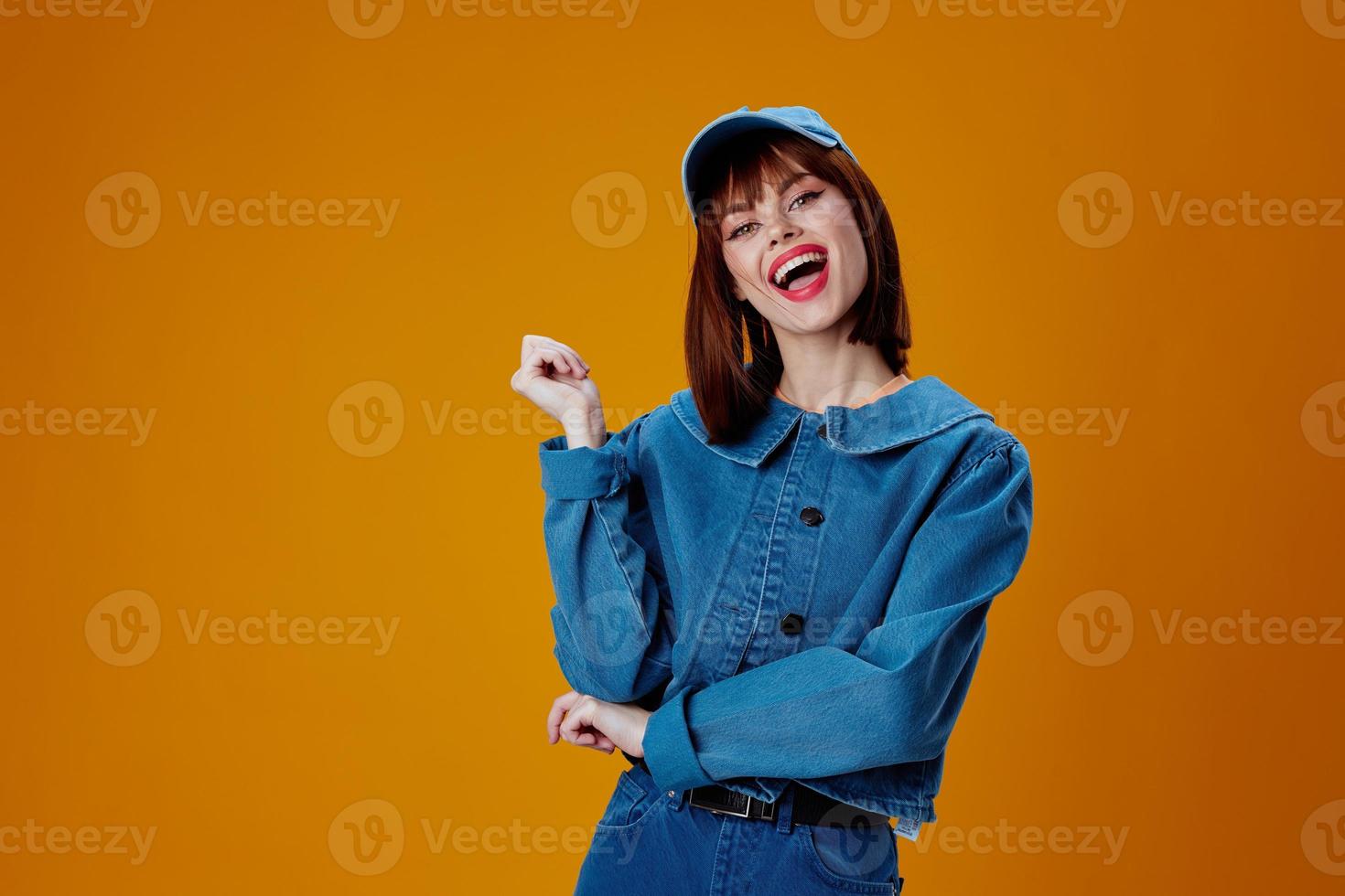 pretty woman in a cap and denim jacket posing yellow background unaltered photo